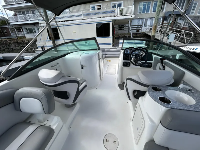 Slide: The Image of 2022 NauticStar 243 DC boat interior with seating and helm, docked near waterfront homes. - 18