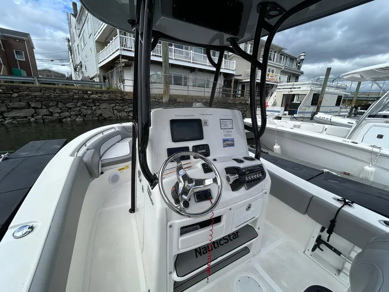 Slide: The Image of 2021 NauticStar 2302 Legacy boat docked by a river under a cloudy sky. - 12
