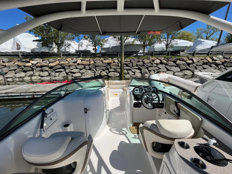 Slide: The Image of 2021 NauticStar 243 DC boat interior with seating and helm, docked by a stone wall. - 28
