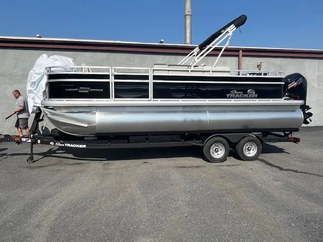 The Image of 2026 Sun Tracker Fishin' Barge 20 DLX pontoon boat on trailer, parked outdoors. - 3