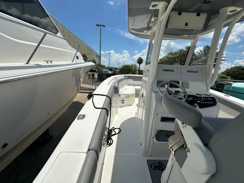 Slide: The Image of 2021 NauticStar 28XS boat interior with helm, seating, and Simrad electronics under a clear sky. - 21