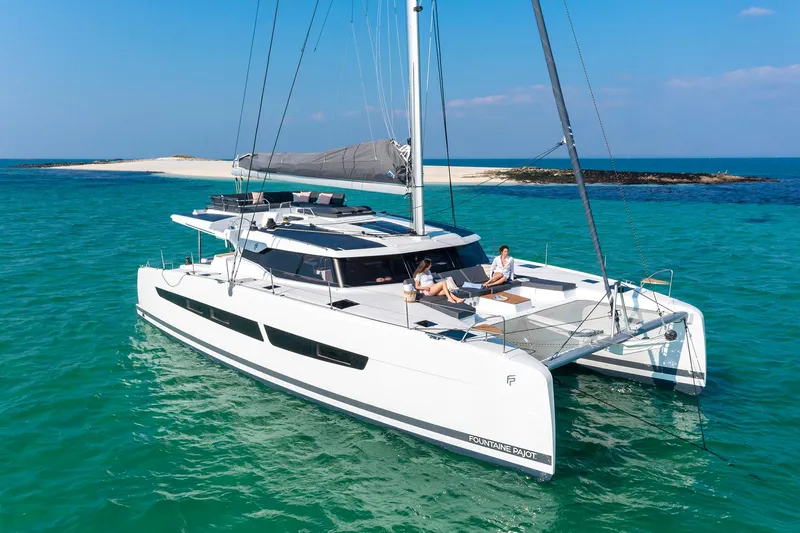 The Image of 2025 Fountaine Pajot Aura 51 catamaran sailing in turquoise waters near a sandy island. - 0