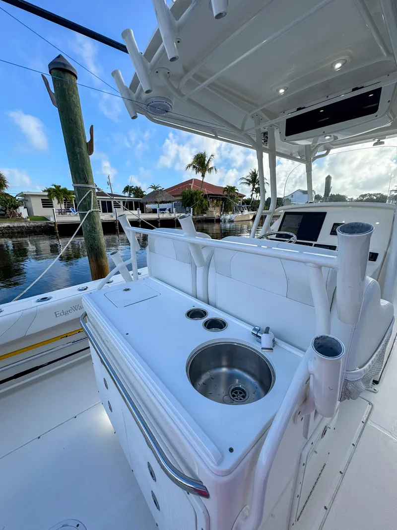 Slide: The Image of 2013 Edgewater 318CC boat interior with sink and rod holders, docked by waterfront homes. - 12
