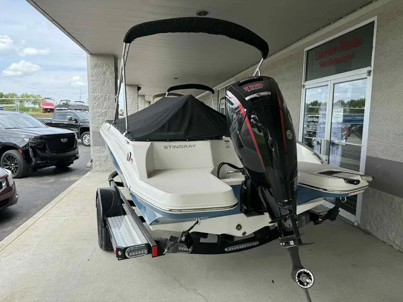 Slide: The Image of 2024 Stingray 182 SC boat with outboard motor, parked at a marina sales department. - 2