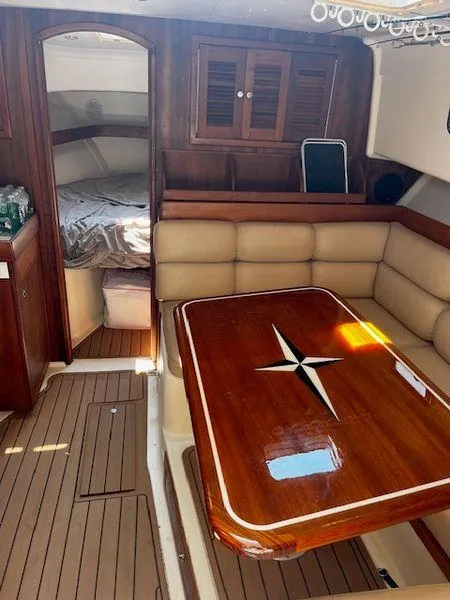 Slide: The Image of 2003 Mainship Pilot 34 interior with wood table, cushioned seating, and cozy sleeping area. - 13