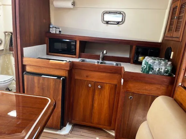 Slide: The Image of 2003 Mainship Pilot 34 interior kitchen with wood cabinetry, sink, microwave, and mini fridge. - 15