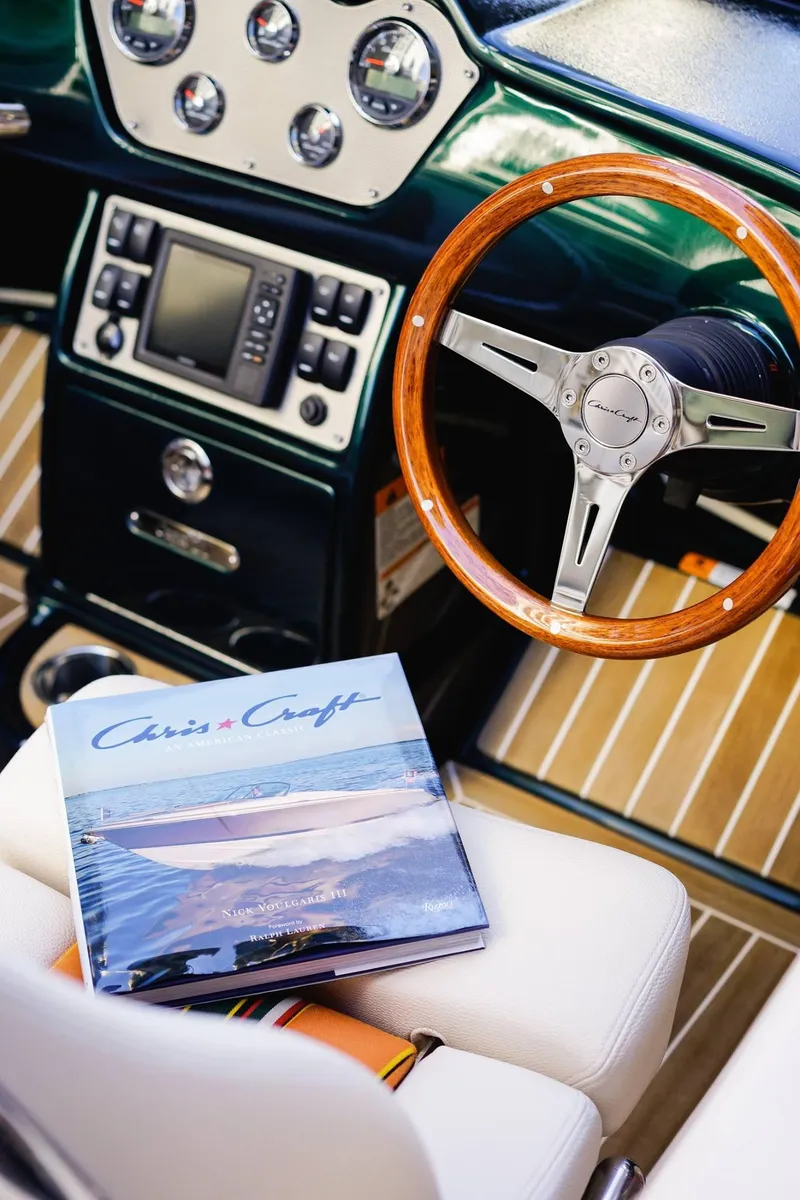 Slide: The Image of 2018 Chris-Craft Capri 21 cockpit with wooden steering wheel and nautical book on seat. - 22
