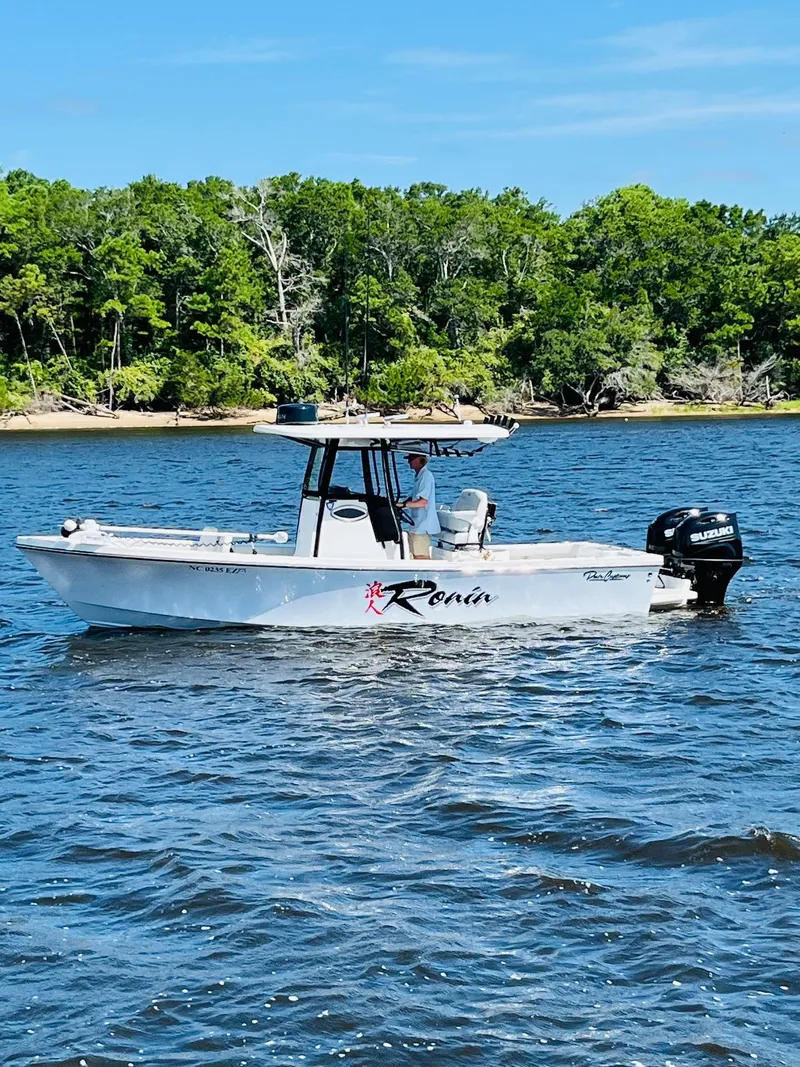 Slide: The Image of 2023 Pair Customs 24 Center Console DV boat cruising under a bridge on a sunny day. - 1