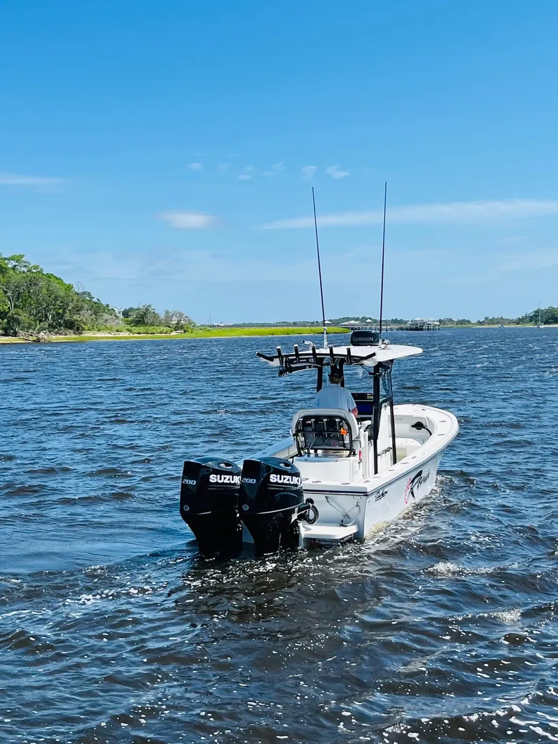 Slide: The Image of 2023 Pair Customs 24 Center Console DV boat cruising under a bridge on a sunny day. - 2