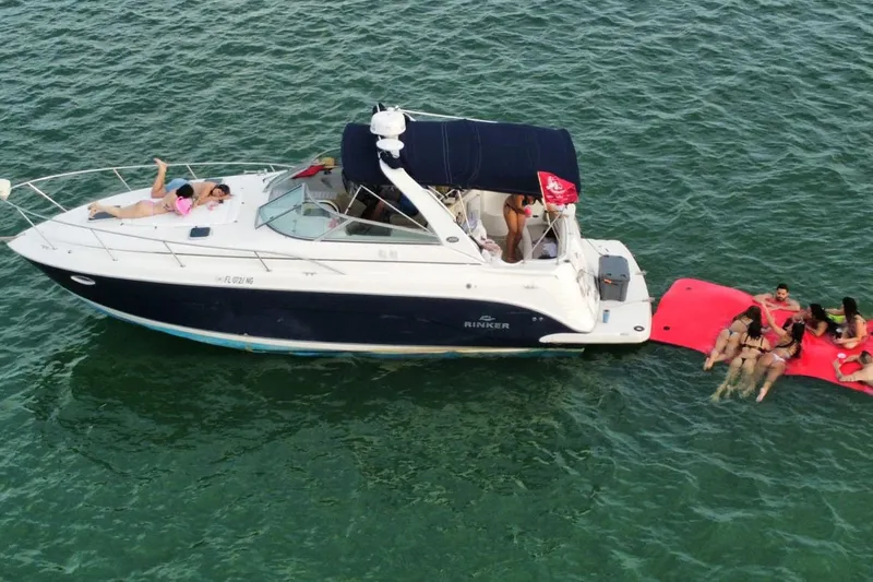 Slide: The Image of 2006 Rinker 300 Express Cruiser on water with people relaxing on deck and floating mat. - 16