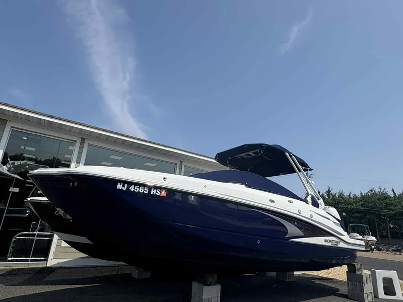 Slide: The Image of 2023 Monterey M65 boat displayed outdoors on blocks, under a clear blue sky. - 2