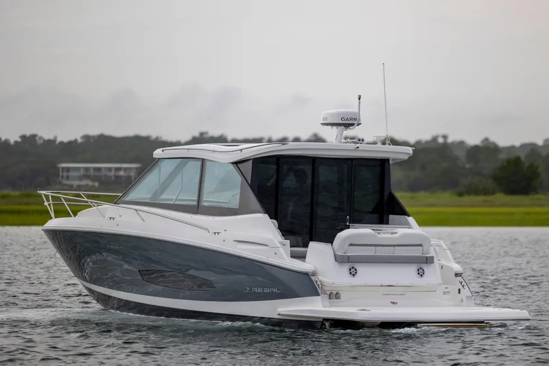 Slide: The Image of 2022 Regal 36 Grande Coupe cruising on a serene lake with lush greenery. - 6