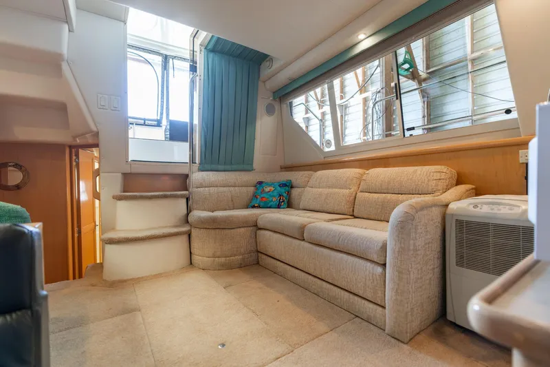 Slide: The Image of 1998 Carver 355 Aft Cabin interior with beige sofa, stairs, and large windows. - 7