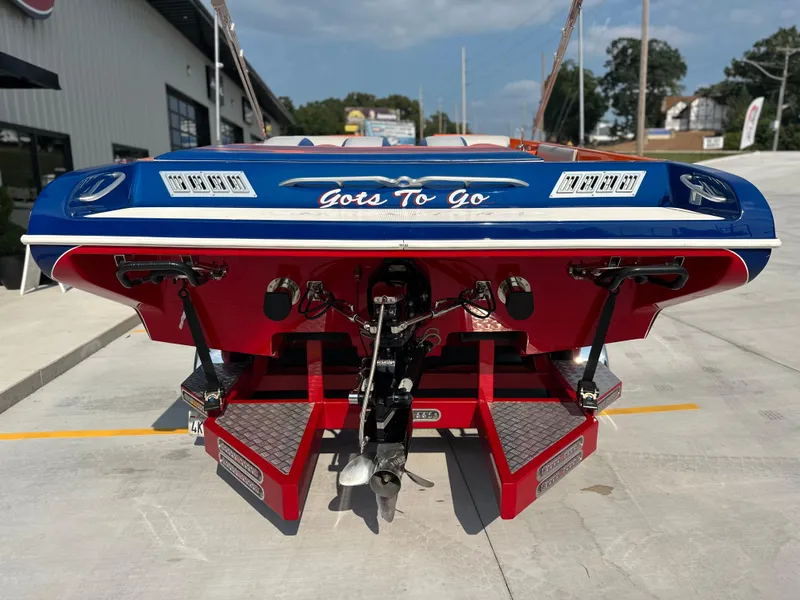 Slide: The Image of 2008 Shockwave Fundeck boat, blue and red, rear view, parked on concrete. - 3