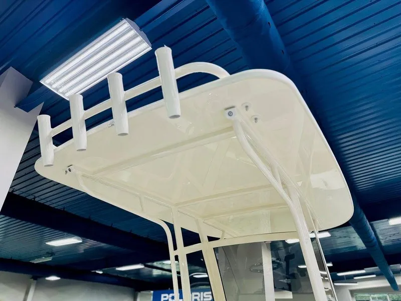 Slide: The Image of 2026 Scout 215 XSF boat T-top with rod holders, under showroom lighting. - 5