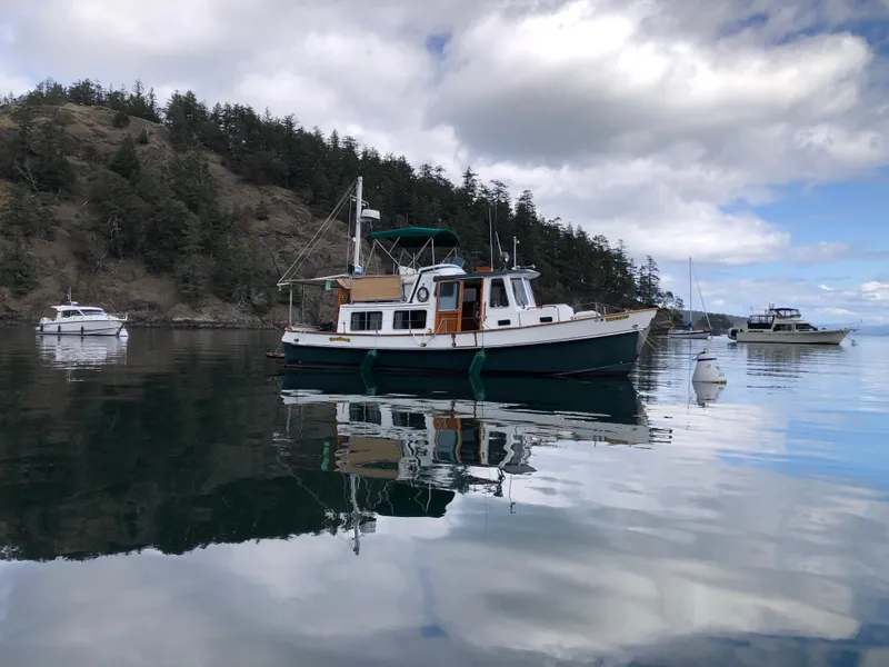 Slide: The Image of 1989 Eagle 32 Trawler anchored in serene waters with forested hills in the background. - 29
