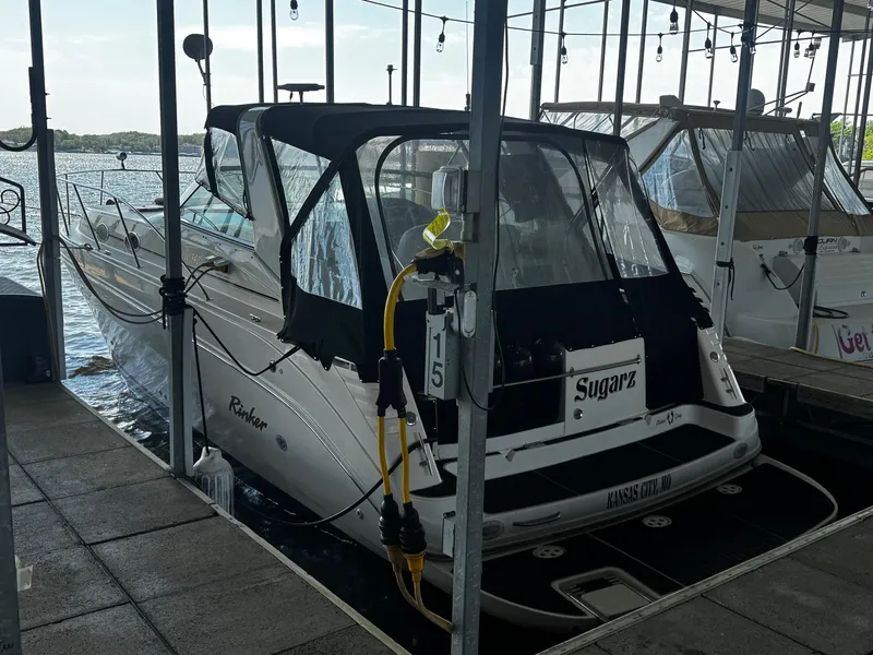 Slide: The Image of 2000 Rinker 340 Fiesta Vee docked in marina, rear view with canopy and water backdrop. - 2