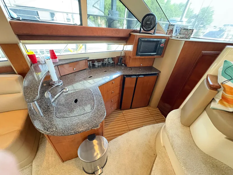 Slide: The Image of 2006 Meridian Fly Bridge Convertible yacht interior with kitchenette, featuring sink, microwave, and wooden cabinetry. - 20