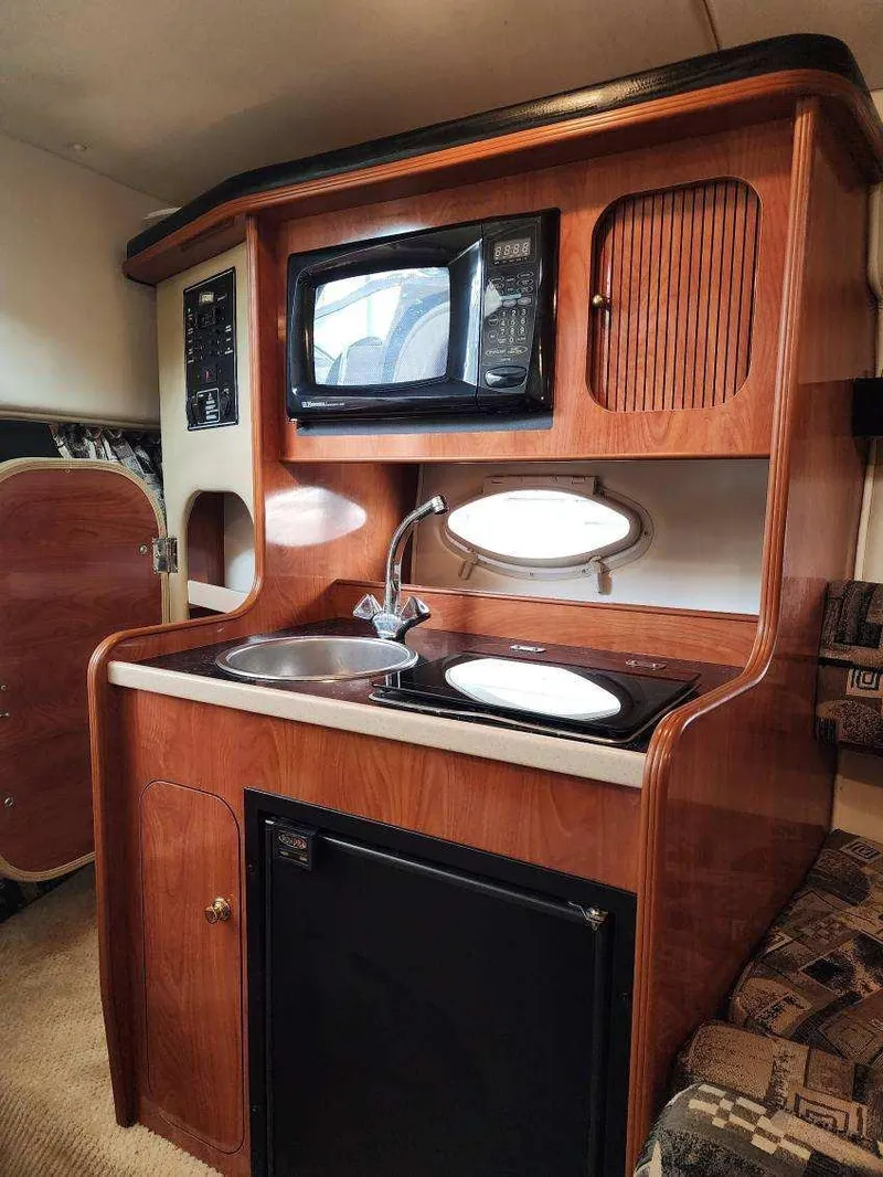 Slide: The Image of 2003 Rinker 270 Express Cruiser interior kitchen with microwave, sink, and compact fridge. - 21