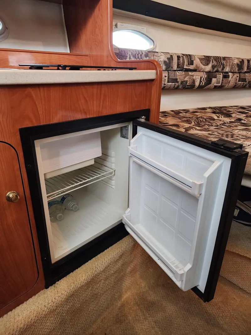 Slide: The Image of Open mini fridge inside 2003 Rinker 270 Express Cruiser cabin, showcasing interior storage space. - 23