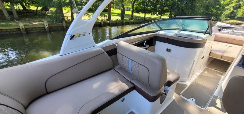 Slide: The Image of 2017 Sea Ray SDX 240 Outboard boat interior with beige seating and scenic river backdrop. - 10