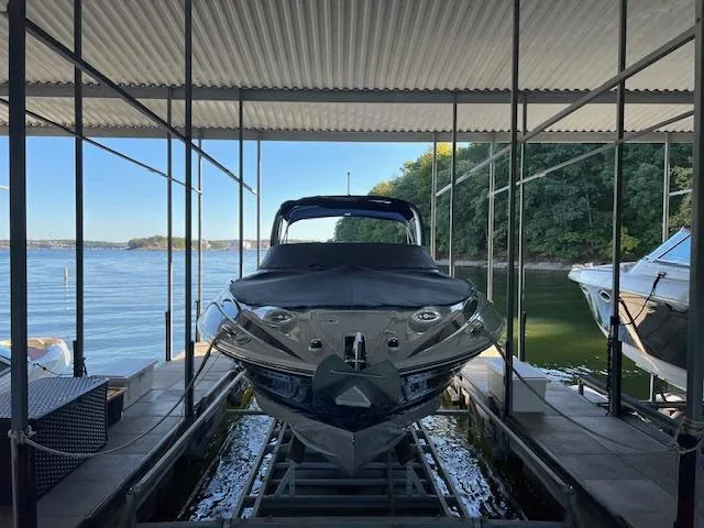 Slide: The Image of 2012 Crownline 325 SS boat docked under a covered structure by a scenic lake. - 2