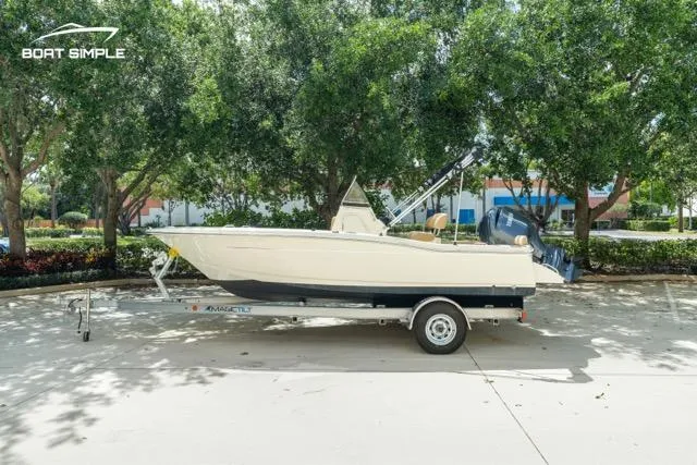 Slide: The Image of 2024 Scout 195 Sportfish boat on trailer, parked outdoors with trees in the background. - 0