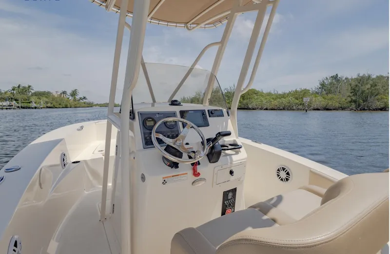 Slide: The Image of 2023 Scout 195 Sportfish boat interior with steering wheel, console, and seating on a calm waterway. - 6