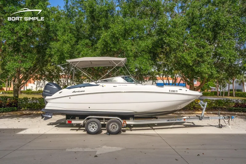Slide: The Image of 2025 Hurricane SunDeck 2400 OB boat on trailer, parked outdoors with trees in background. - 6