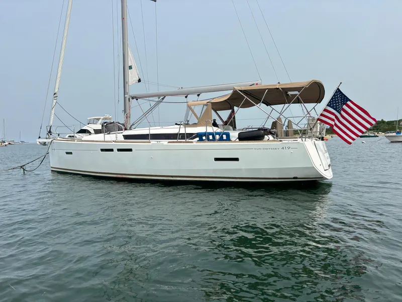 Slide: The Image of 2019 Jeanneau Sun Odyssey 419 sailboat with American flag on calm water. - 1