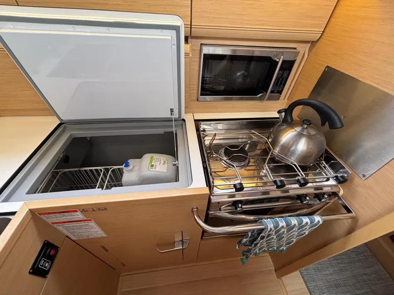 Slide: The Image of Galley of 2019 Jeanneau Sun Odyssey 419 with stove, kettle, and open fridge. - 38