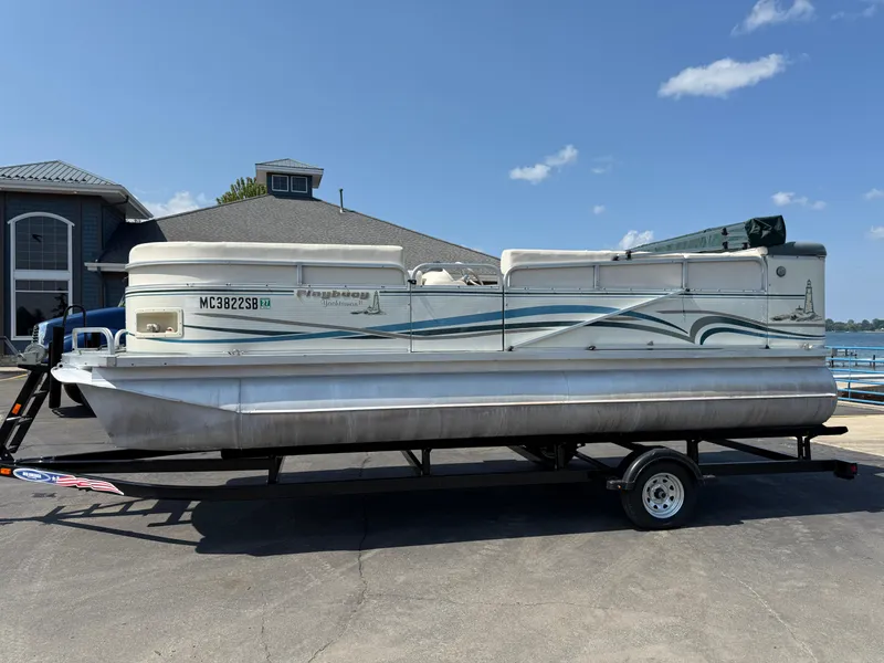 Slide: The Image of 2000 Playbuoy Yachtsman 21 pontoon boat on trailer, parked near waterfront building. - 1
