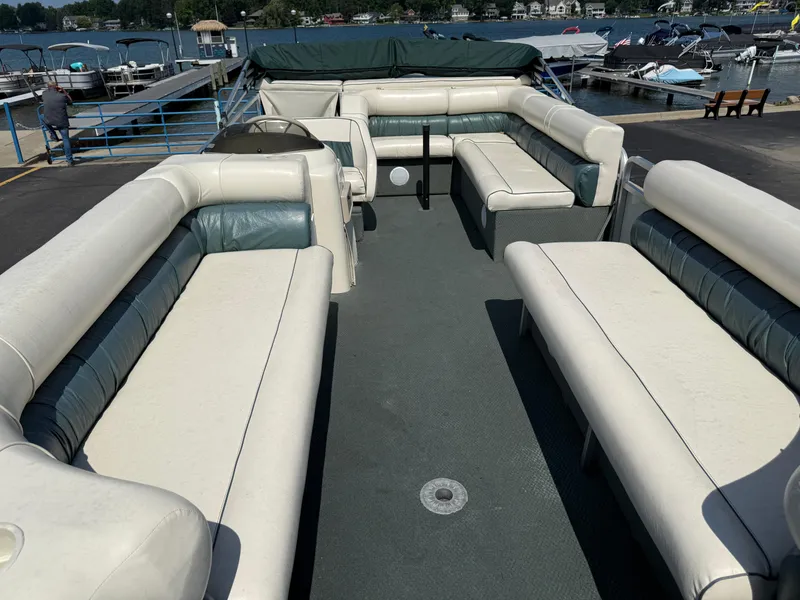 Slide: The Image of Pontoon boat interior with white seating, docked by a lake. Playbuoy Yachtsman 21, 2000 model. - 7