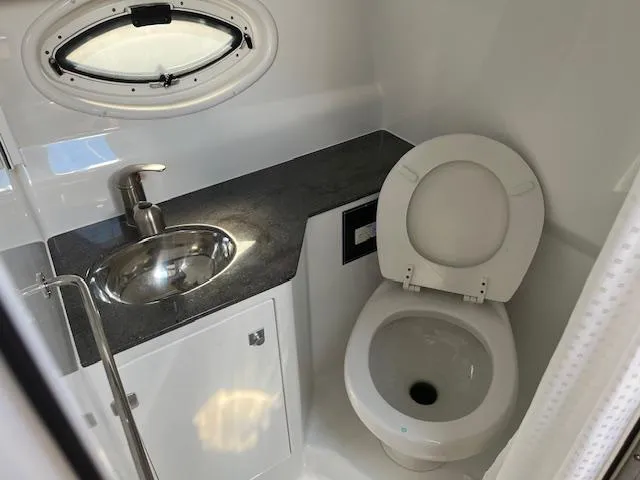 Slide: The Image of 2022 Monterey 295 Sport Yacht bathroom with sink, toilet, and porthole window. - 24