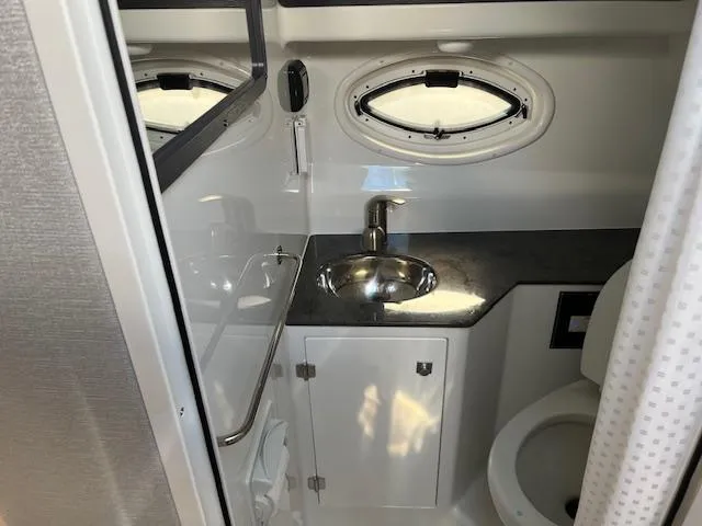 Slide: The Image of 2022 Monterey 295 Sport Yacht bathroom with sink, mirror, and porthole window. - 25