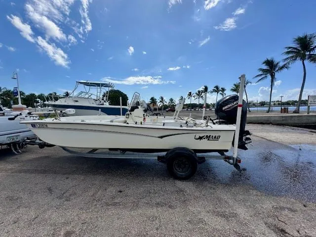 Slide: The Image of 2023 Mako Pro Skiff 17 CC boat on trailer, parked near palm trees under blue sky. - 2