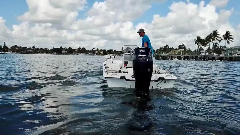 Slide: The Image of 2023 Mako Pro Skiff 17 CC on water, with person steering, under a partly cloudy sky. - 6