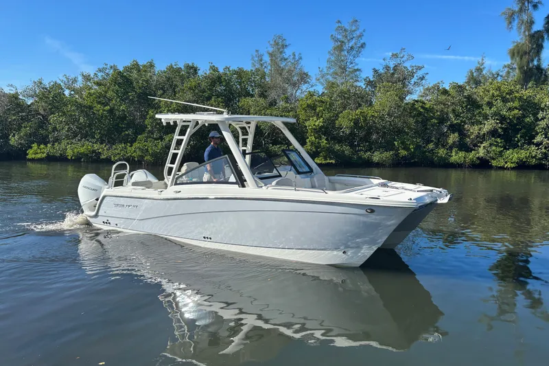 Slide: The Image of 2026 World Cat 265 DC-X boat cruising on a calm river with lush greenery. - 2