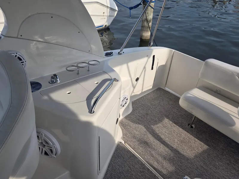 Slide: The Image of 2004 Sea Ray 280 Sundancer boat interior with seating and control panel, docked by the water. - 10