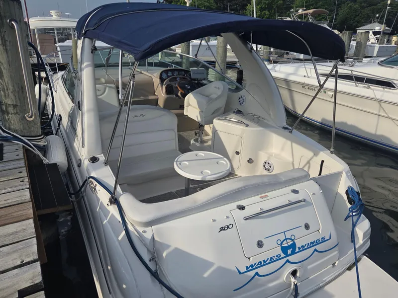 Slide: The Image of 2004 Sea Ray 280 Sundancer boat docked, featuring a blue canopy and spacious seating area. - 5
