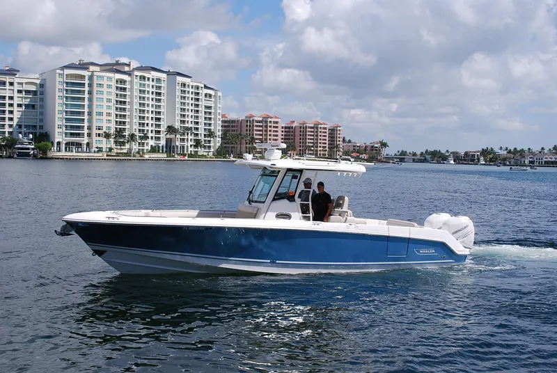 The Image of 2017 Boston Whaler 330 Outrage boat cruising near waterfront buildings under cloudy sky. - 0