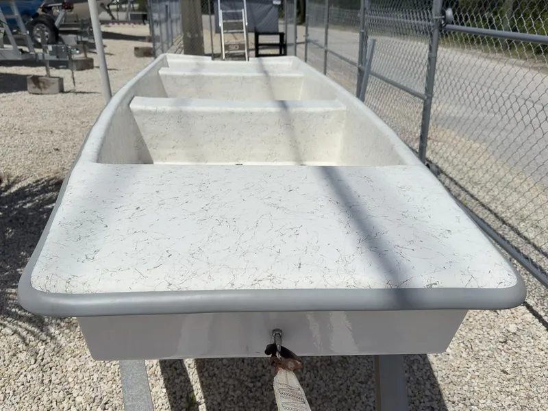 Slide: The Image of 2026 Coastal Skiff 145 boat, white interior, parked on gravel near chain-link fence. - 12