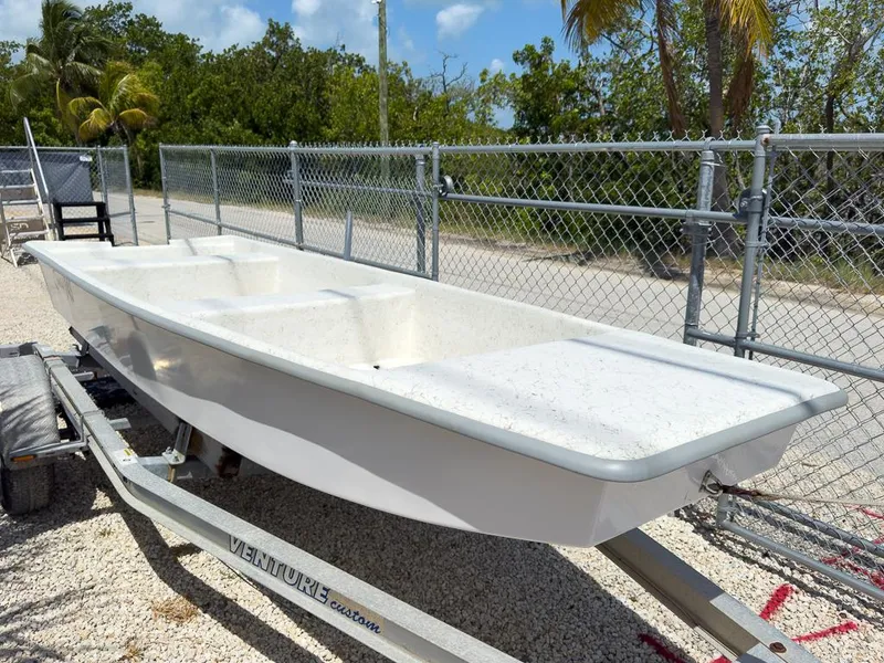 Slide: The Image of 2026 Coastal Skiff 145 boat on trailer, parked near chain-link fence and palm trees. - 8