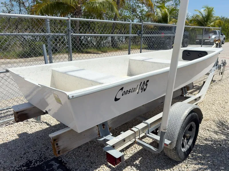 Slide: The Image of 2026 Coastal Skiff 145 boat on trailer, parked near chain-link fence and palm trees. - 9