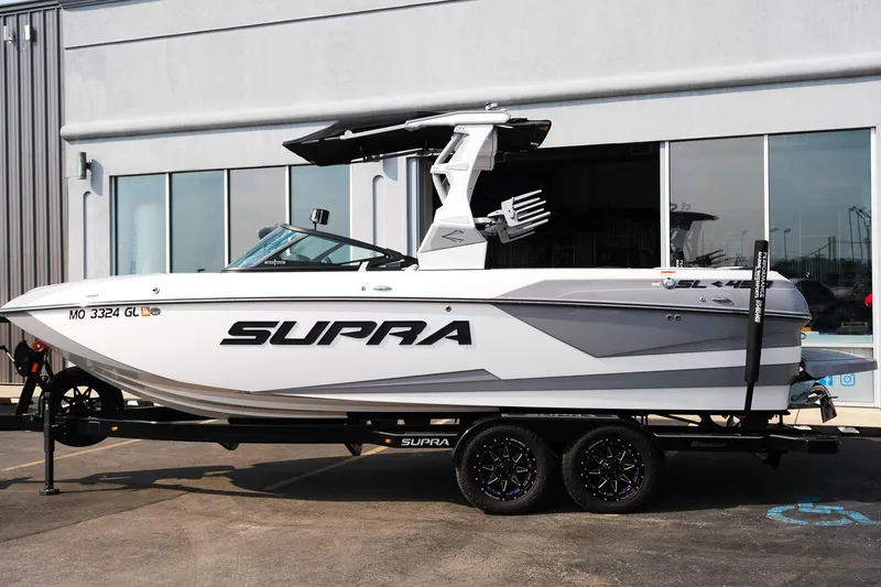Slide: The Image of 2020 Supra SL450 boat on trailer, parked outside a building. - 2