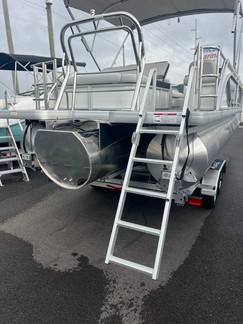 Slide: The Image of 2026 Sweetwater 2286SFLC pontoon boat with ladder on trailer, parked outdoors. - 2