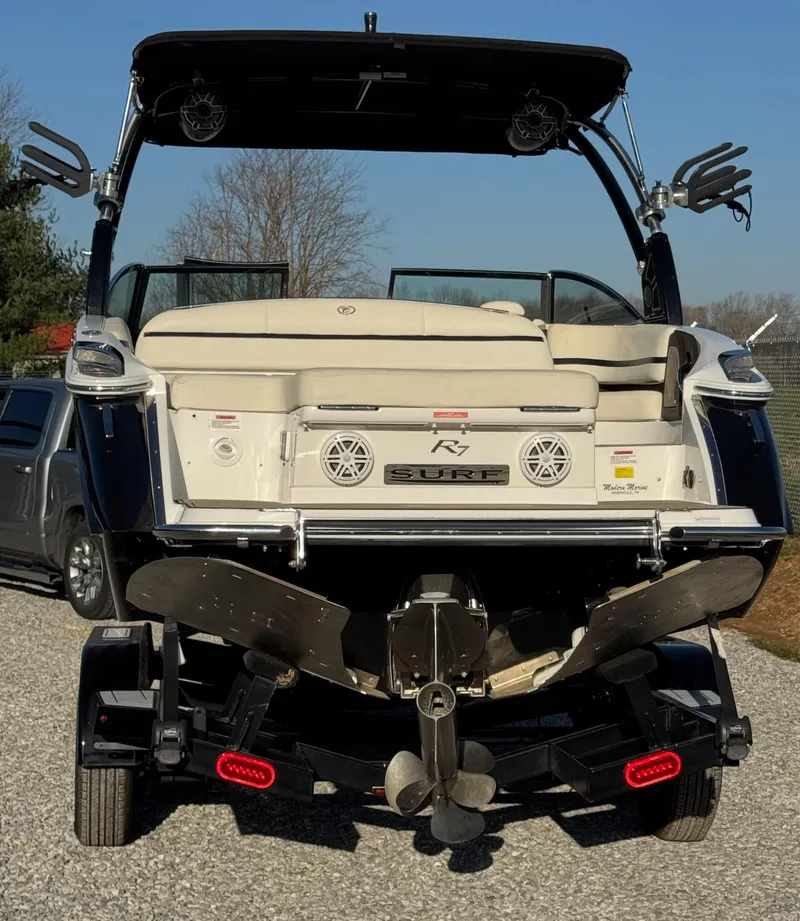 Slide: The Image of 2020 Cobalt R7 Surf boat rear view with propeller and speakers, parked on gravel. - 1