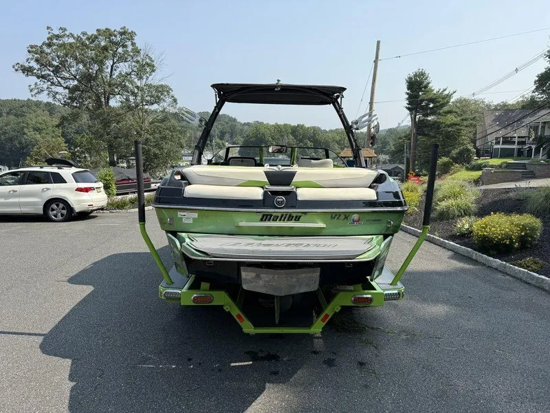 Slide: The Image of 2015 Malibu 22 VLX boat in parking lot, green exterior, surrounded by trees and cars. - 2