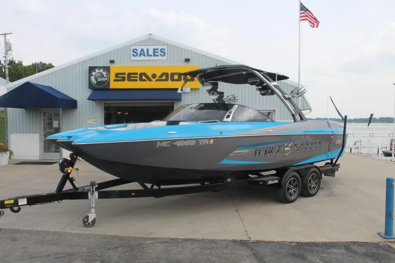 The Image of 2013 Malibu Wakesetter 24 MXZ boat on trailer outside dealership with American flag. - 1
