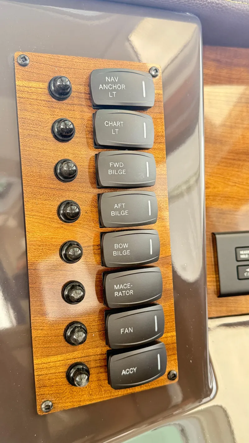 Slide: The Image of Control panel of 2026 Ranger Tugs R-27 with labeled switches on wood finish. - 26